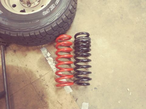 1996 Ford Bronco - Two suspension springs, one red and one black, are shown next to a tire, likely for a vehicle's front suspension.
