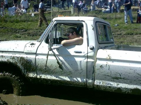 1995 Ford Bronco - A white pickup truck is stuck in the mud, with a driver visible inside.