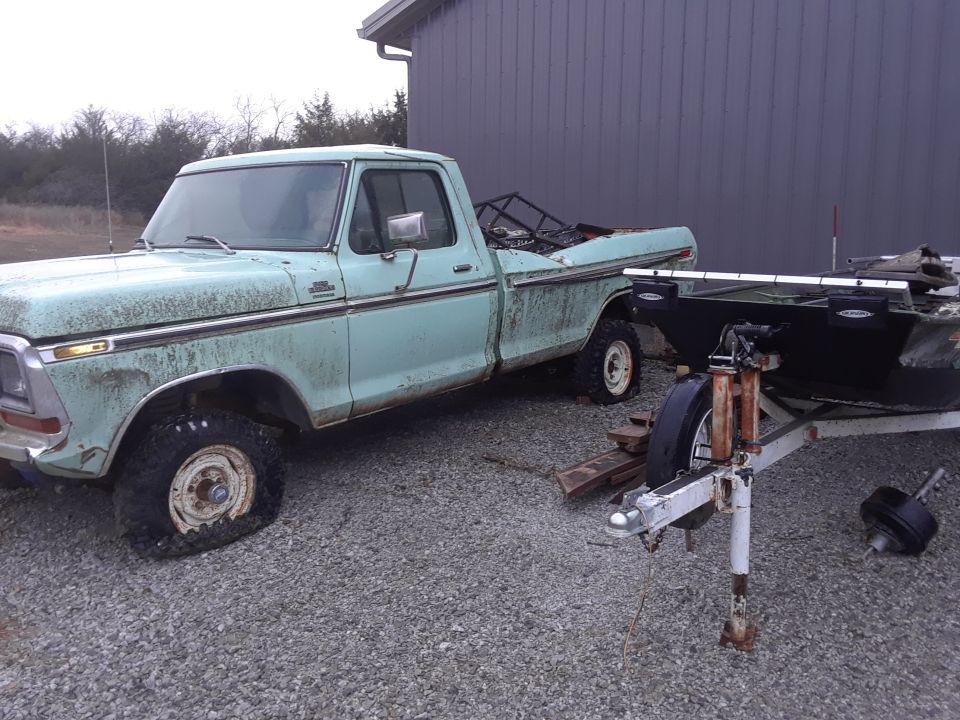 Light blue 1977 Ford F-150 pickup truck with a flat front tire, parked next to a boat on a trailer