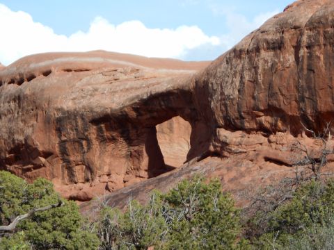 1992 Ford Bronco - A natural archway carved into sandstone cliffs, surrounded by arid vegetation under a partly cloudy sky.