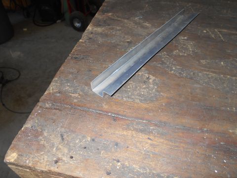 1992 Ford Bronco - A metal trim piece rests on a worn wooden surface in a workshop setting.