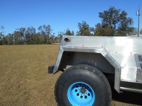 1992 Ford Bronco - A custom aluminum vehicle body is shown from the side, a bright blue wheel and a grassy field in the background.