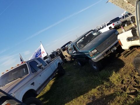 1996 Ford Bronco - Two Ford trucks are parked on a grassy field under a clear blue sky.