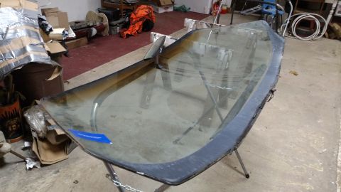 1979 Chevrolet Camaro - A detached windshield rests on a stand in a cluttered garage setting, awaiting installation.