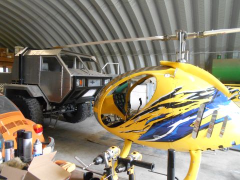 1992 Ford Bronco - Workshop scene with a custom armored vehicle, helicopter fuselage, and an orange VW Beetle.