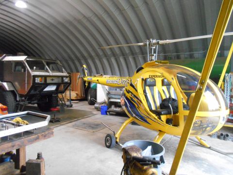 1992 Ford Bronco - A yellow helicopter and a custom-built truck are parked inside a large, industrial-style garage.