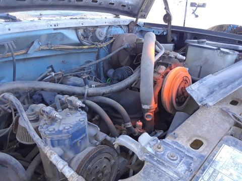 1994 Ford Bronco - The engine bay of a light blue vehicle shows various components and hoses.