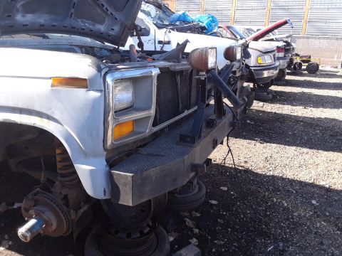 1994 Ford Bronco - This truck, possibly a Ford F-Series or Bronco from the 1980s, sits in a junkyard with its hood open and missing parts.
