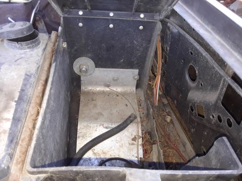 1994 Ford Bronco - The battery tray area of a vehicle shows some rust and debris, with wiring and a hose present.