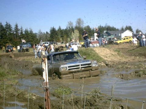 1995 Ford Bronco - A muddy Dodge pickup truck is stuck in a mud bog with spectators watching.