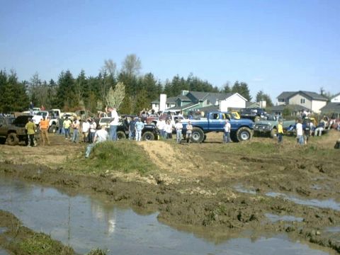 1995 Ford Bronco - Several off-road vehicles are parked in a muddy area with spectators watching.