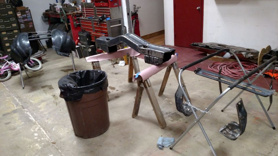 Car parts on sawhorses in a garage, with a trash can and a bicycle nearby