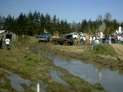 1995 Ford Bronco - A group of trucks are gathered in a muddy field, with spectators observing the off-road activity.