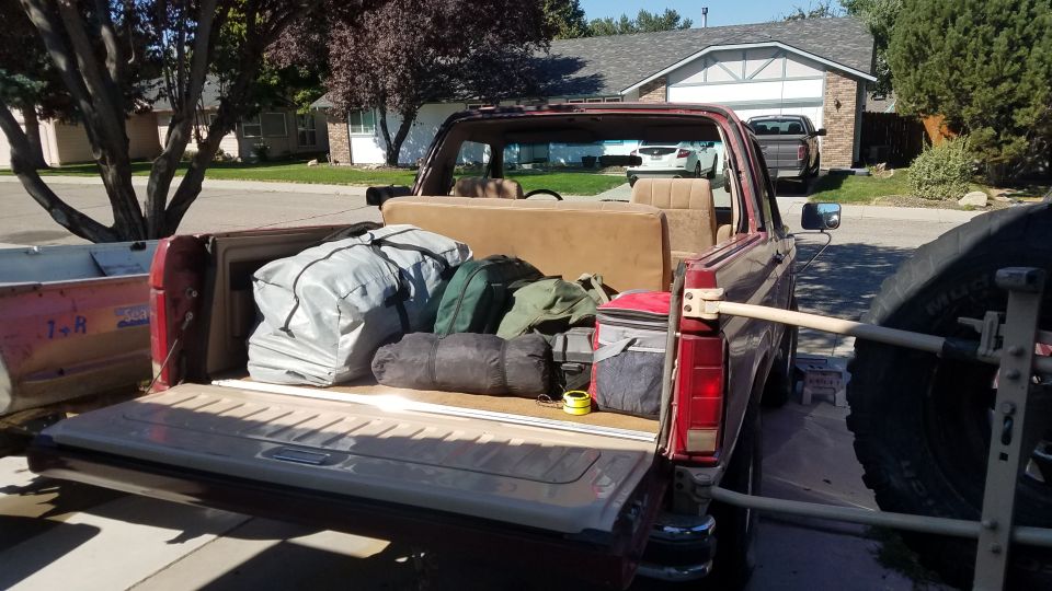 Red Ford Bronco with tailgate down, loaded with camping gear and a cooler; spare tire mounted on rear