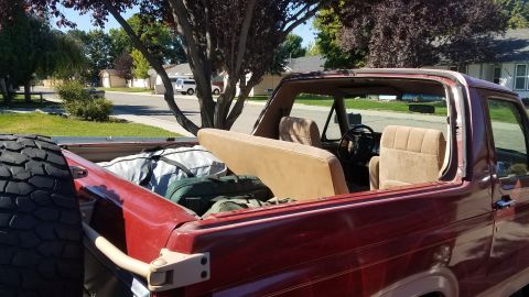 1985 Ford Bronco - Rear view of a red SUV, possibly from the 1980s, with its cargo area loaded with bags and luggage.