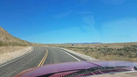1985 Ford Bronco - Driving on a remote highway through a desert environment with sparse vegetation and distant hills.