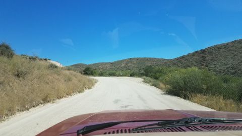 1985 Ford Bronco - View from inside a vehicle driving on a dusty road through a dry, hilly landscape.