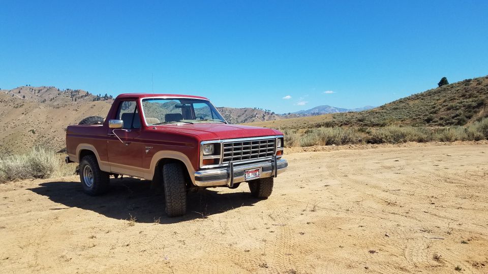 Red Ford Bronco parked on a dirt road with hills and blue sky in the background