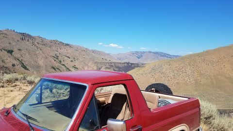 1985 Ford Bronco - A red 1985 Ford Bronco is parked with a view of rolling hills and a clear blue sky.