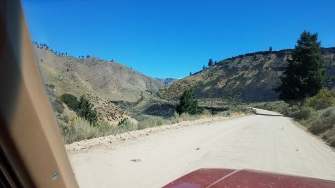 1985 Ford Bronco - Driving on a dirt road through a mountainous landscape under a clear blue sky.