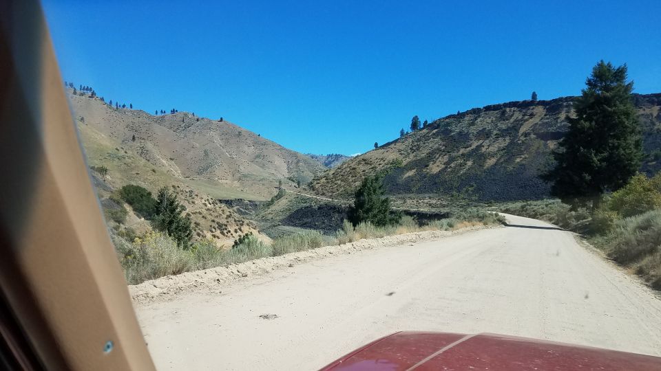 Red vehicle dashboard and hood on a dirt road with mountains and blue sky