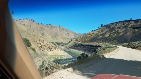 1985 Ford Bronco - Driving through a scenic canyon with a river alongside a dirt road.
