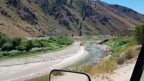 1985 Ford Bronco - View from a vehicle's side mirror shows a river winding through a dry, mountainous terrain.