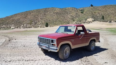 1985 Ford Bronco - This Ford Bronco is parked in a dry, barren landscape under a clear blue sky.
