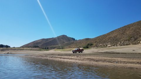 1985 Ford Bronco - A red 1980s SUV drives across a dry lake bed with mountains in the background.