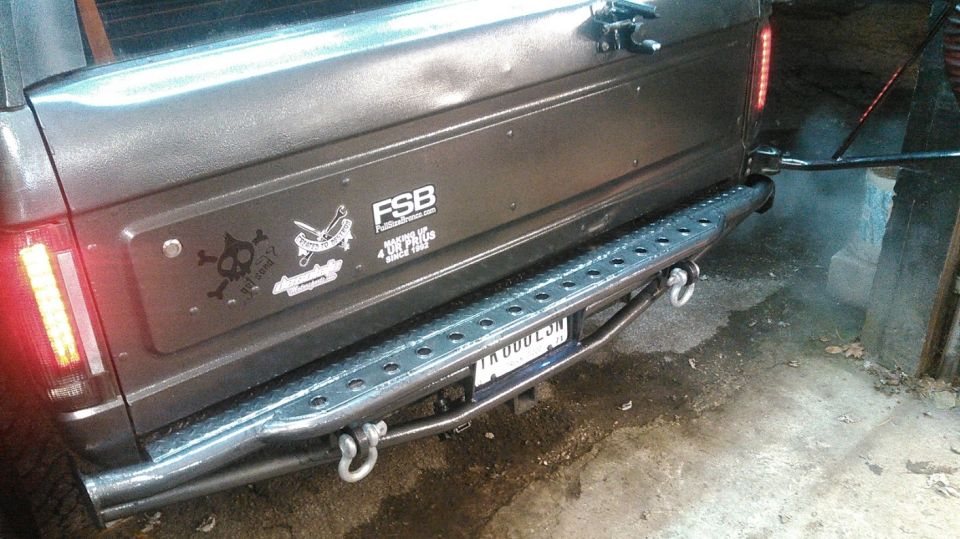 Bare metal tube rear bumper with diamond plate step on a gray SUV tailgate