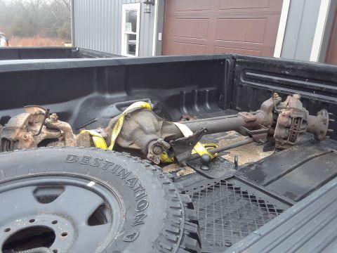 1994 Ford Bronco - Spare tire and rear axle assembly secured with yellow straps in the bed of a pickup truck.