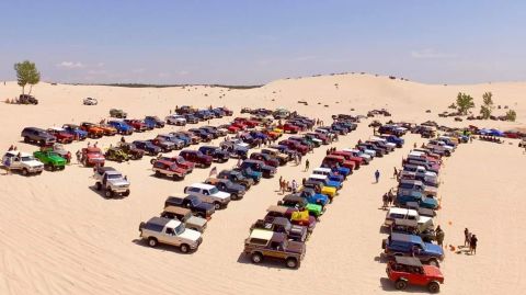1996 Ford Bronco - A large gathering of Ford Broncos are parked in rows on a sandy terrain.