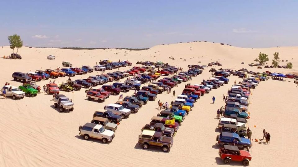Multiple Ford Broncos parked on sand dunes under a clear sky