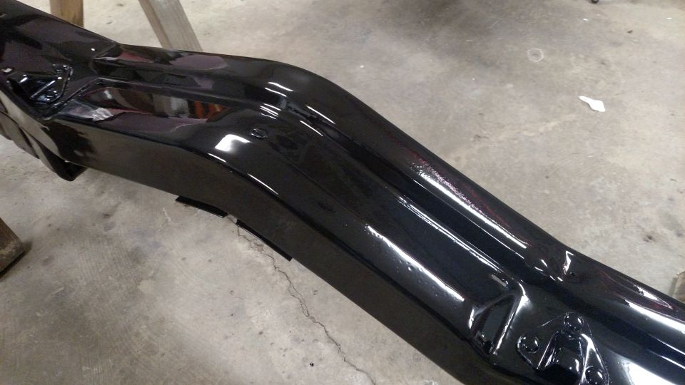 Glossy black car bumper, possibly aftermarket, mounted on sawhorses