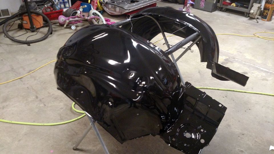 Black painted car fenders and wheel wells on a stand, with a vacuum cleaner and bicycle in the background