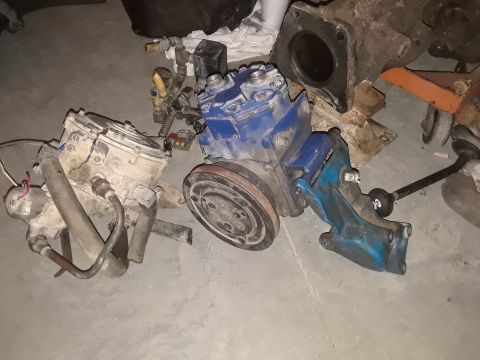 1994 Ford Bronco - Assorted vehicle parts, including two air conditioning compressors, are laid out on a floor.