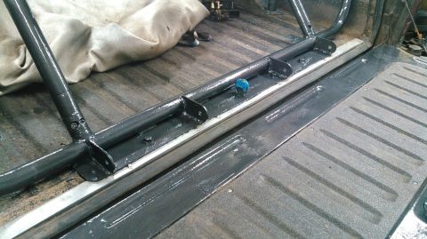 1978 Ford Bronco - Close-up view of a custom roll cage installed in the bed of a truck, with visible mounting hardware and dark grey tubing.
