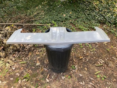 1996 Ford Bronco - A gray rear spoiler is shown resting on a black trash can in an outdoor setting with foliage in the background.