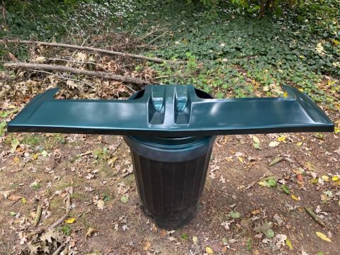 1996 Ford Bronco - A green car part is displayed outdoors, resting on a dark trash receptacle.