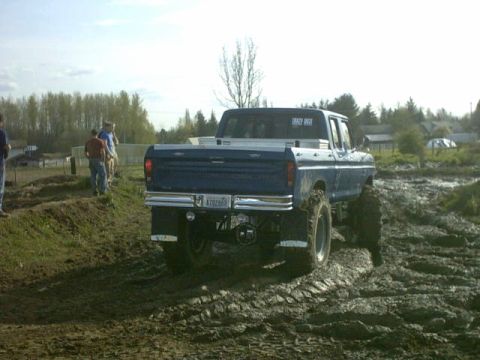 1995 Ford Bronco - This lifted blue pickup truck appears to be stuck in a muddy field, with its rear end prominently displayed.
