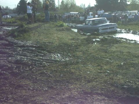 1995 Ford Bronco - A classic Ford truck is stuck in a mud pit during an event, with onlookers gathered.