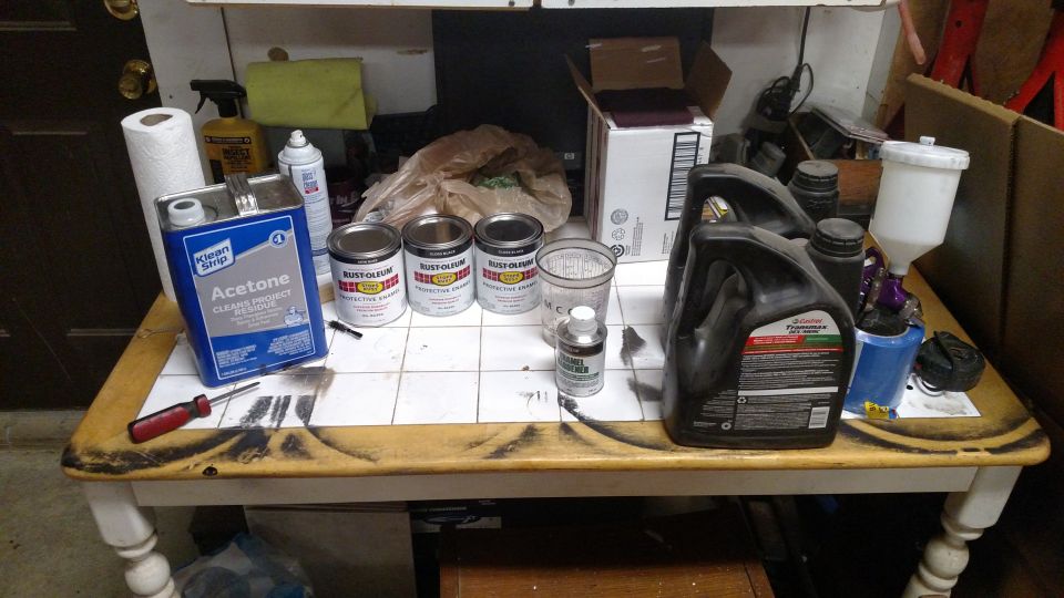 Table with acetone, cans of Rust-Oleum, oil jugs, and a spray gun