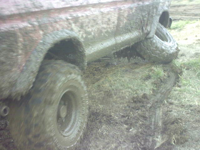 Truck side and tires completely caked in thick mud over rutted ground