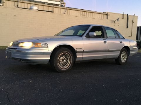 1994 Ford Crown Victoria - Silver sedan parked on asphalt with headlights on, viewed from the front 3/4 angle.