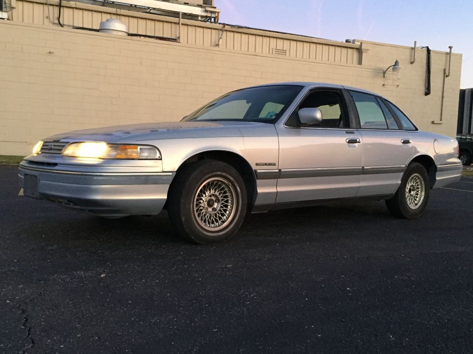 Silver sedan parked on asphalt, front 3/4 view. Headlights are on