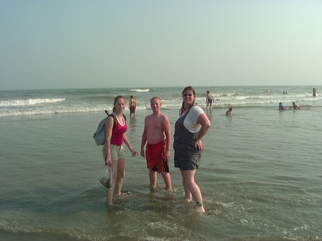 Three people stand in shallow ocean water with waves behind them