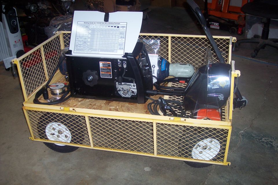 Yellow wire mesh trailer with welding equipment, including a welder, helmet, and wire spool