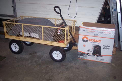 1995 Ford Bronco - A yellow utility wagon filled with items sits beside a box for a Hobart Handler 210MVP welding machine.