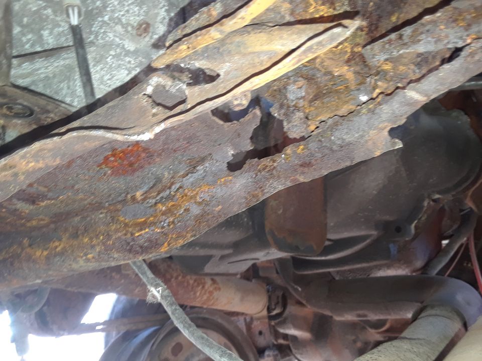 Heavily rusted frame rails and suspension parts of an old vehicle