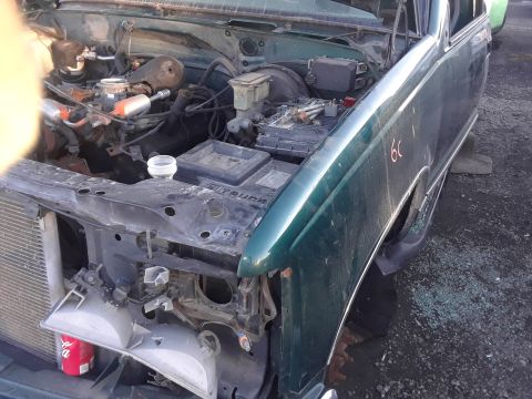 1994 Ford Bronco - The engine bay of a green truck is visible with the hood open, revealing the engine and damaged front end components.